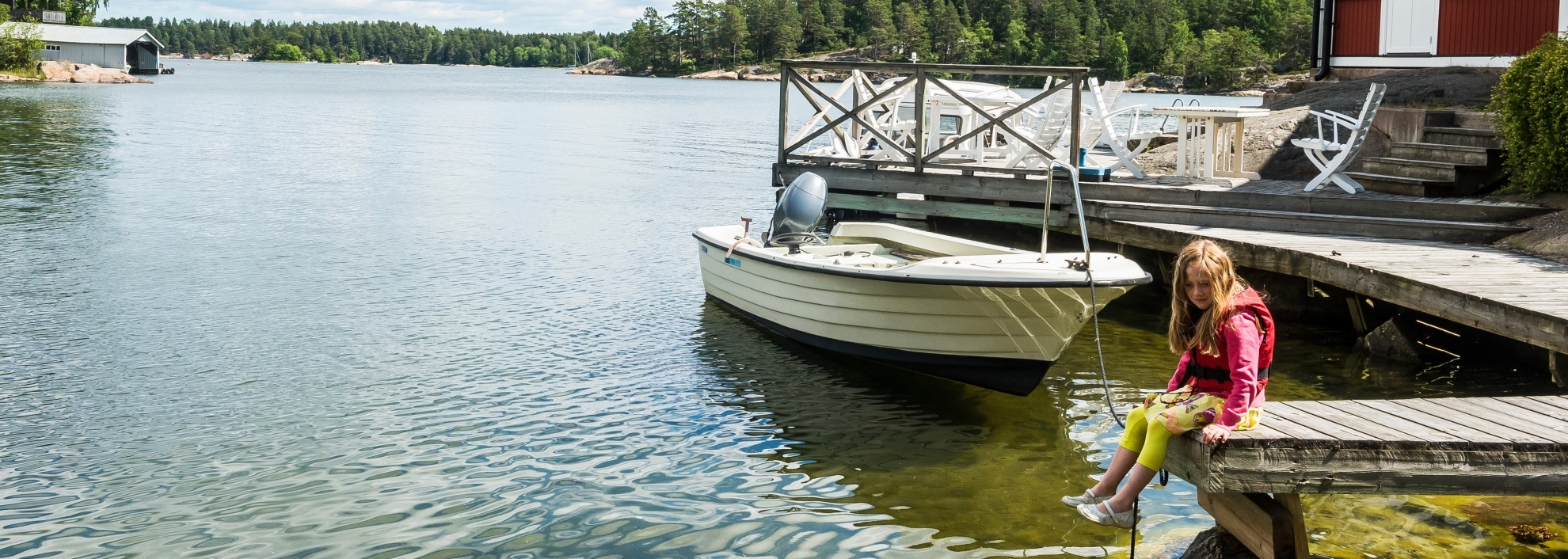 Girl sitting on dock next to boat overlooking lake